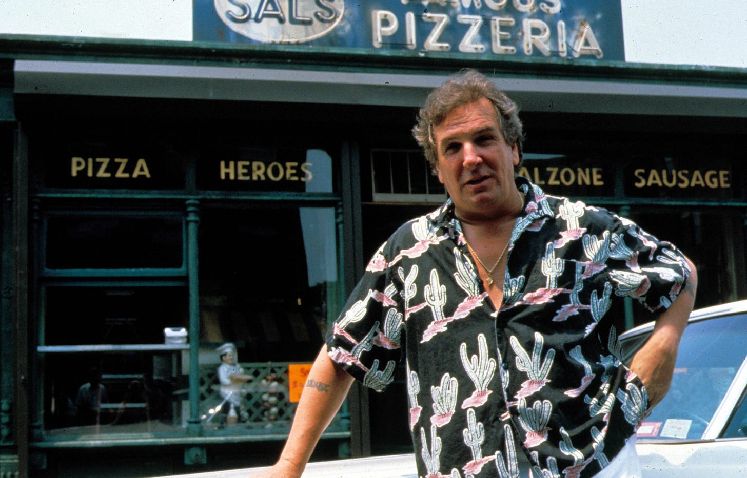 This image shows Sal Frangione (played by Danny Aiello), proprietor of Sal's Famous Pizzeria in Spike Lee's 1989 film Do the Right Thing, standing outside his pizza shop and in front of his Cadillac.