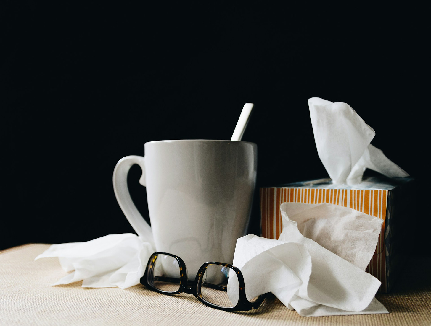 A cup of hot tea, box of tissues, and glasses