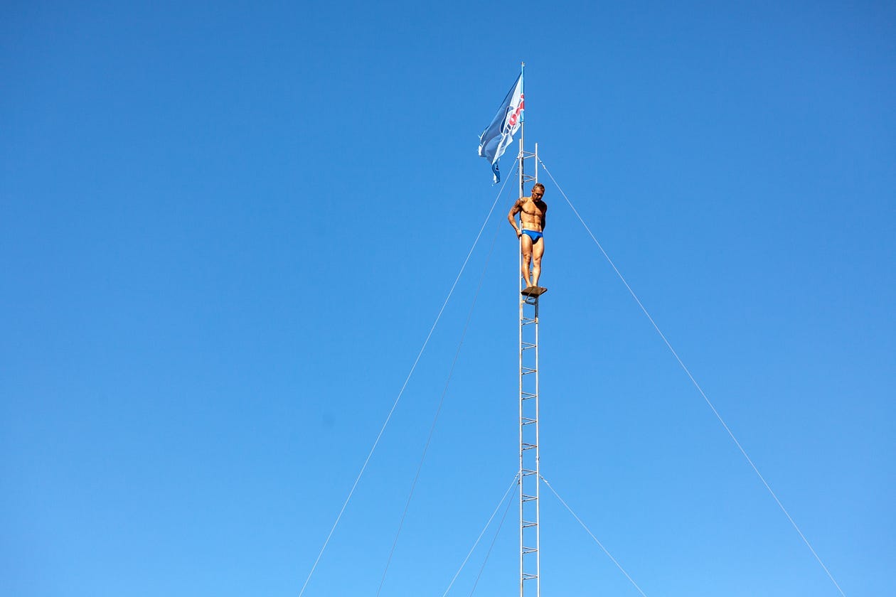 a man standing on a high flagpole in swimwear, looking down