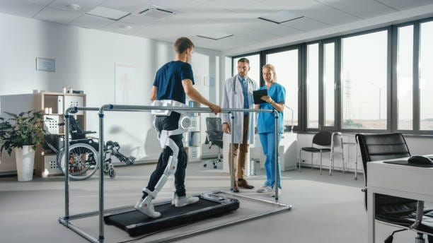 Modern Hospital Physical Therapy: Patient with Injury Walks on Treadmill Wearing Advanced Robotic Exoskeleton. Physiotherapy Rehabilitation Scientists, Engineers, Doctors use Tablet Computer to Help Modern Hospital Physical Therapy: Patient with Injury Walks on Treadmill Wearing Advanced Robotic Exoskeleton. Physiotherapy Rehabilitation Scientists, Engineers, Doctors use Tablet Computer to Help ehabilitation Robotics stock pictures, royalty-free photos & images