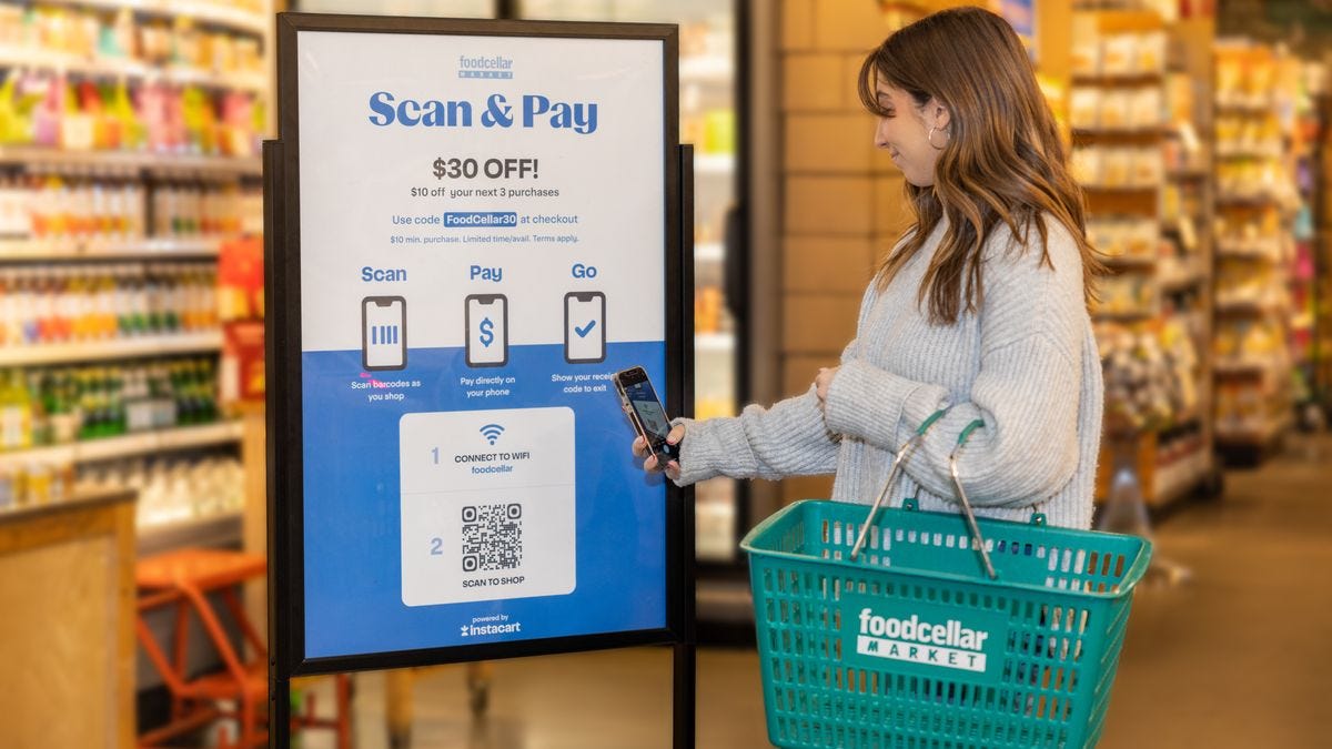 A customer in front of a promotional sign for a scan and pay solution at a grocery store.