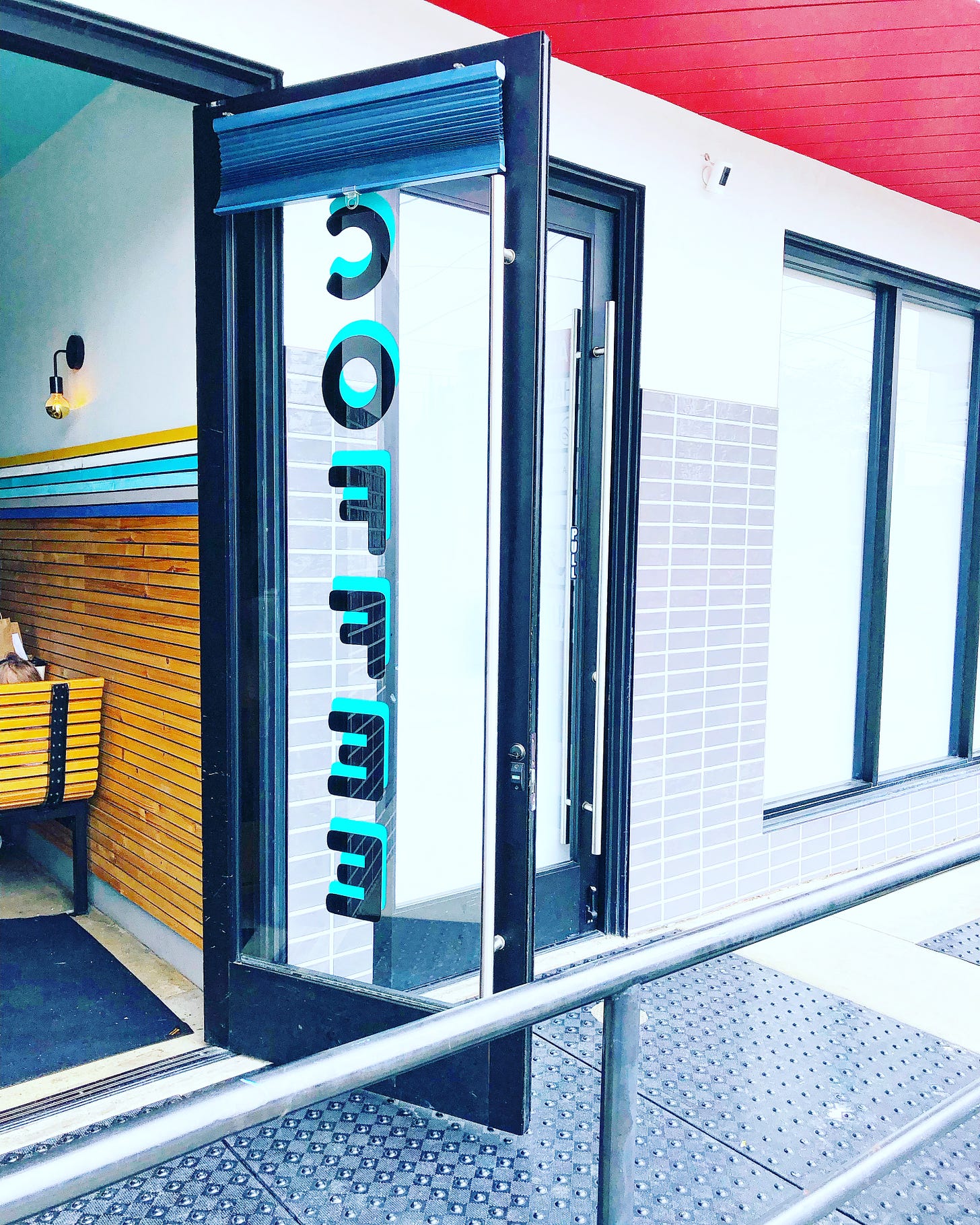 Open door with the word "coffee" written vertically in black and teal amidst a red ceiling.