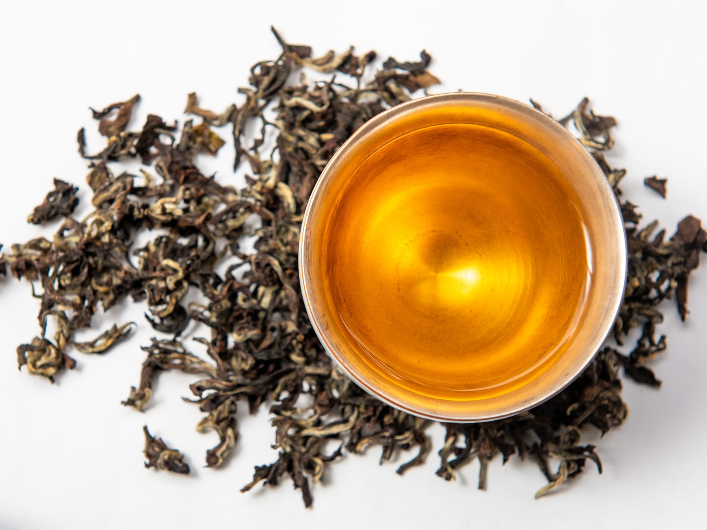 ID: Champagne oolong brewed tea in a silver cup, against dry leaf