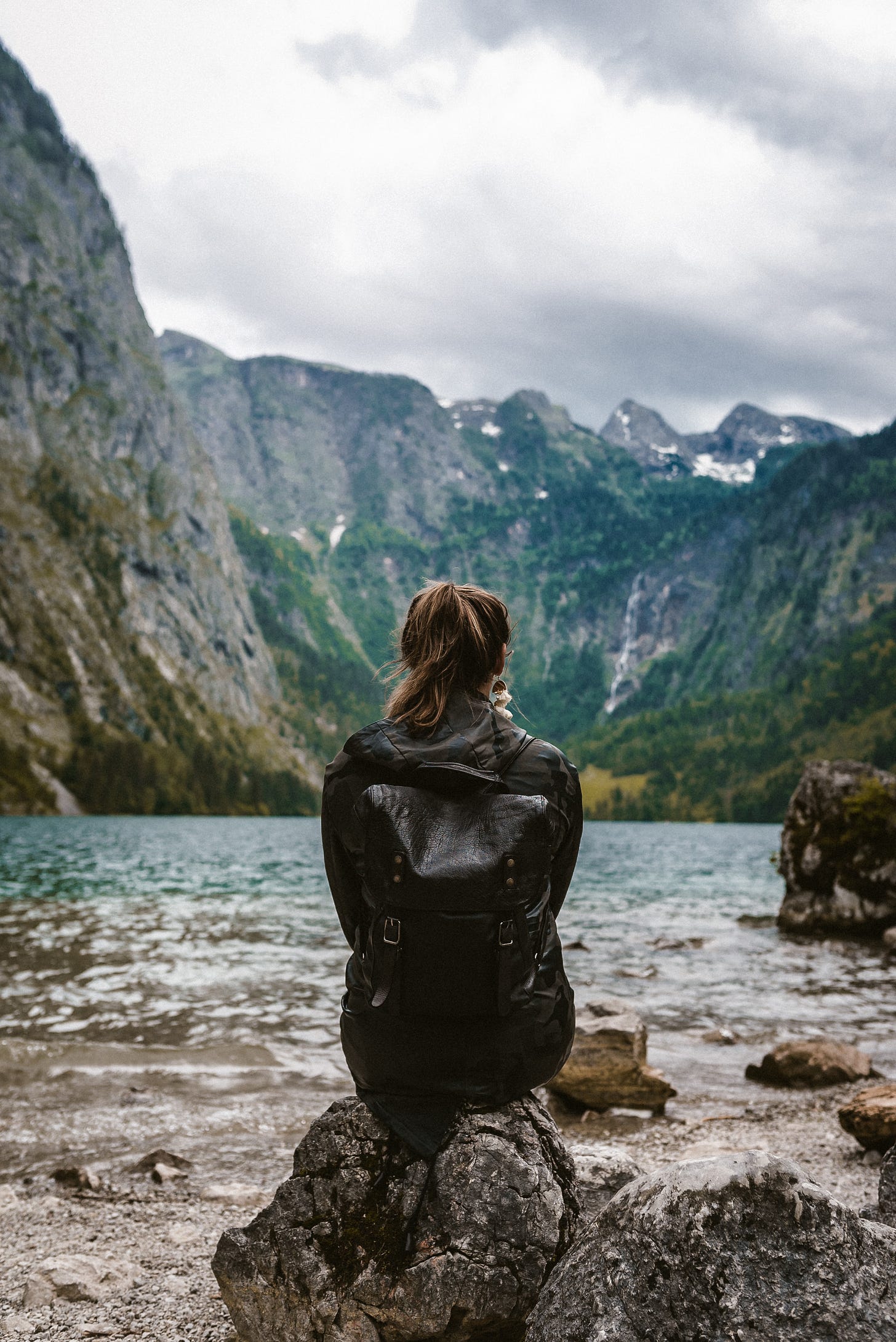 Woman sitting on rocks quietly observing water and mountains