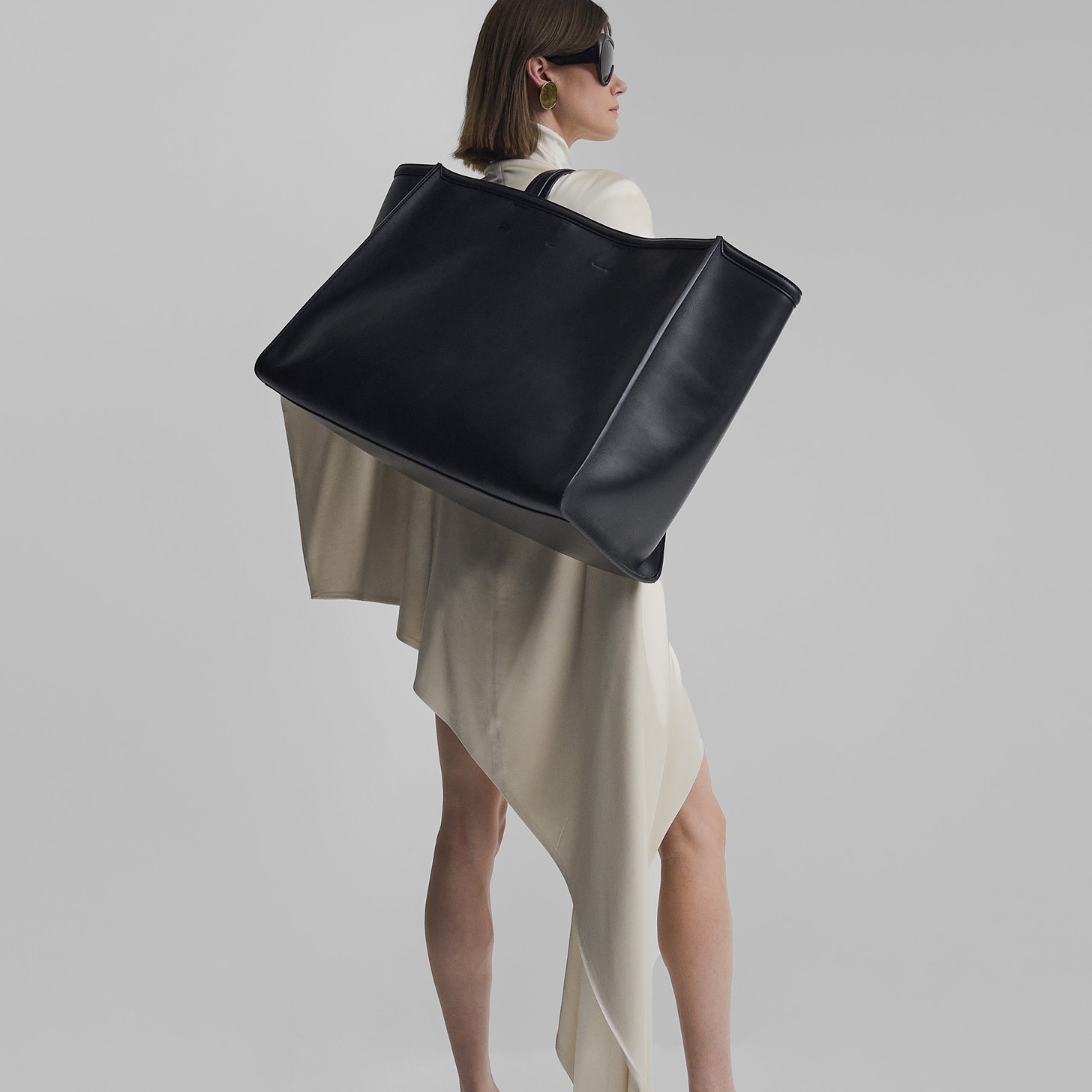 Model holding black leather XL cabas bag. She is wearing a white dress and sunglasses.