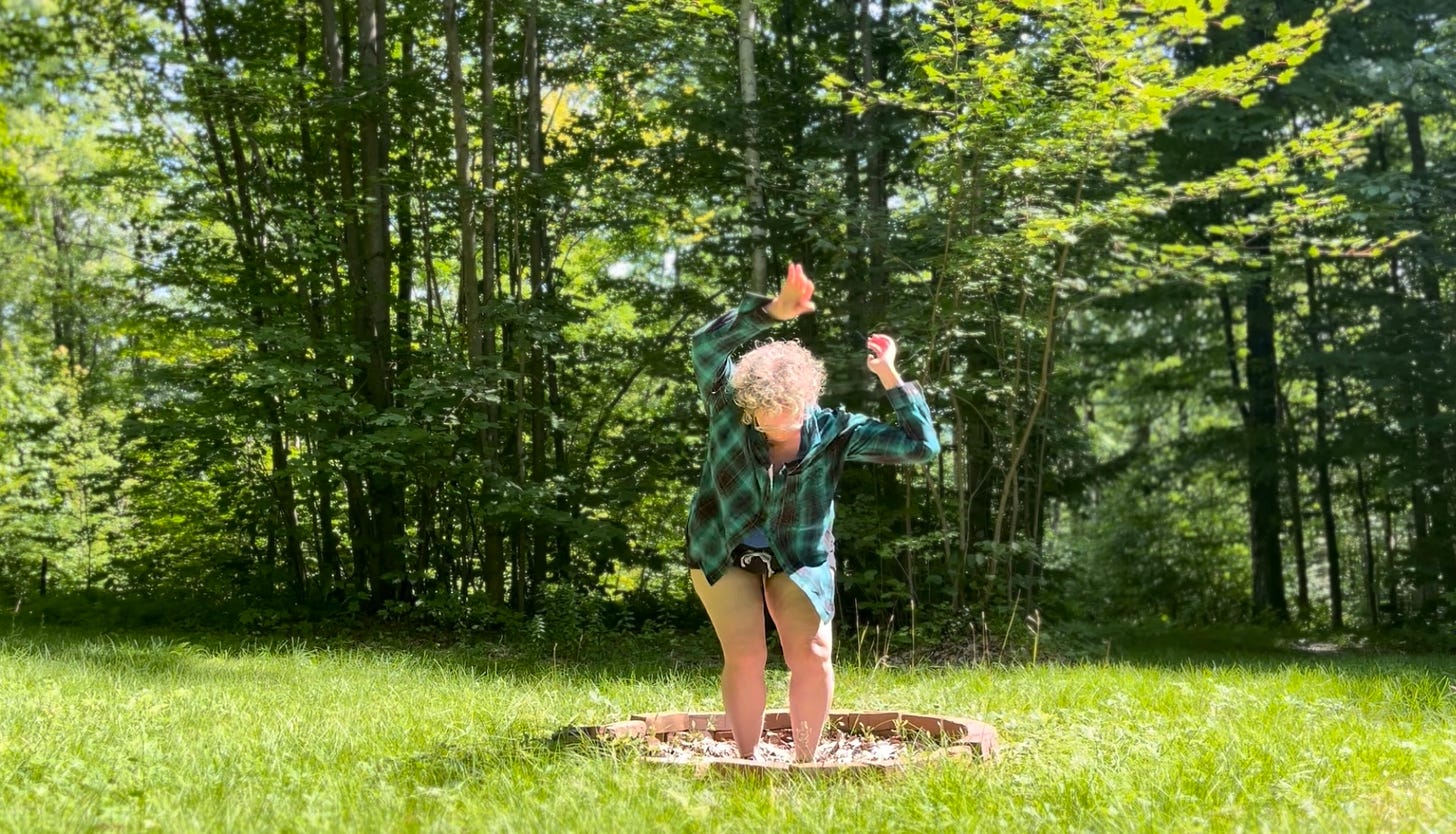 a person in motion in an unlit fire pit with a lush green wood in the background