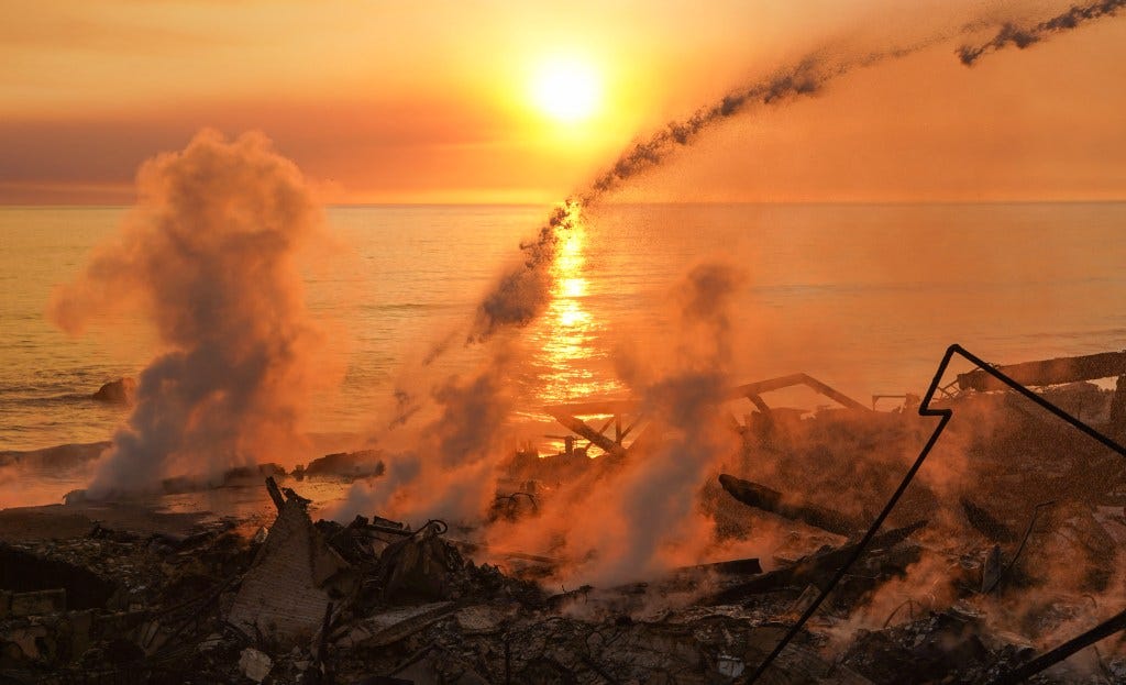 The smouldering wreck of houses, with the sun setting over the sea visible in the background. 