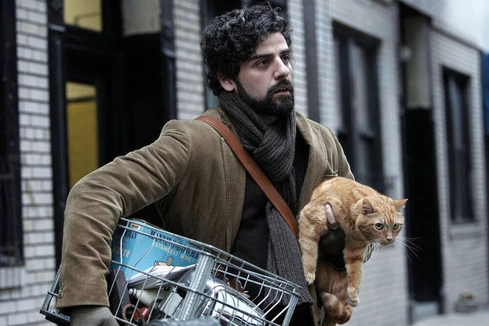 Davis on the street in a brown coat carrying a box and a cat