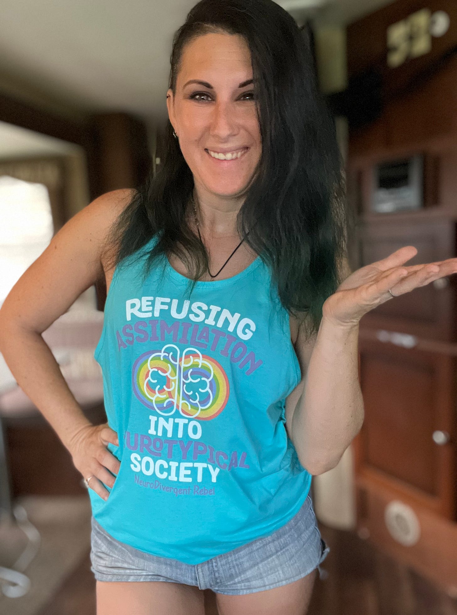 Lyric posing in a teal tank top that says refusing assimilation into Neurotypical society
