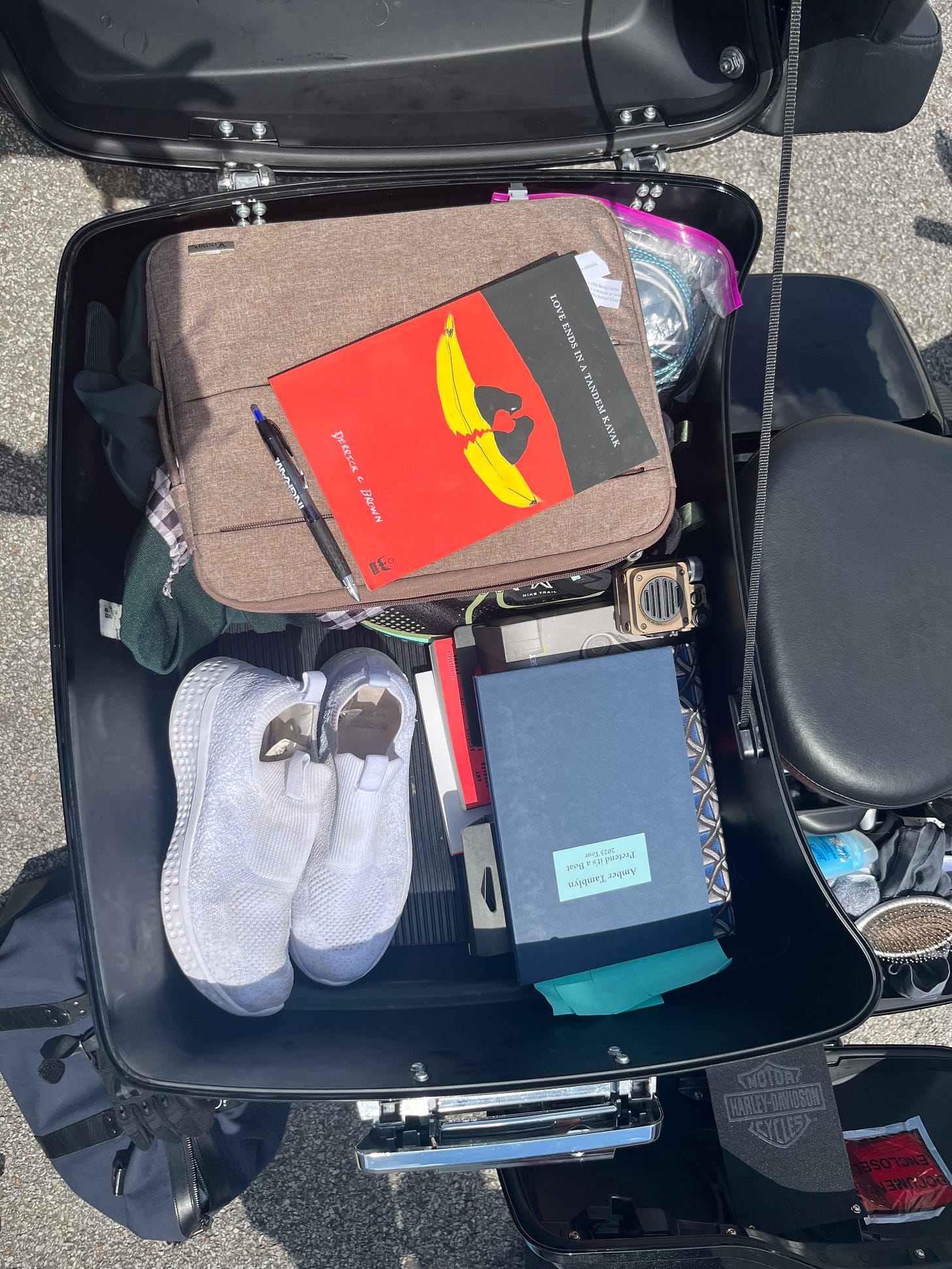 An overhead view of the inside of the storage compartment on the motorcycle. In it are Amber and Derrick's books, a pair of sneakers, and some folded clothes.