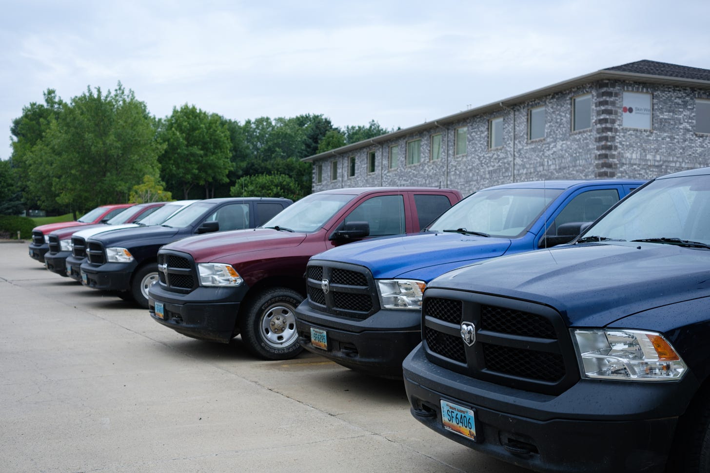 seven Dodge Ram pickups parked snouts-out: Red, maroon, white, navy, cobalt and black. At the North Dakota Department of Mineral Resources. 
