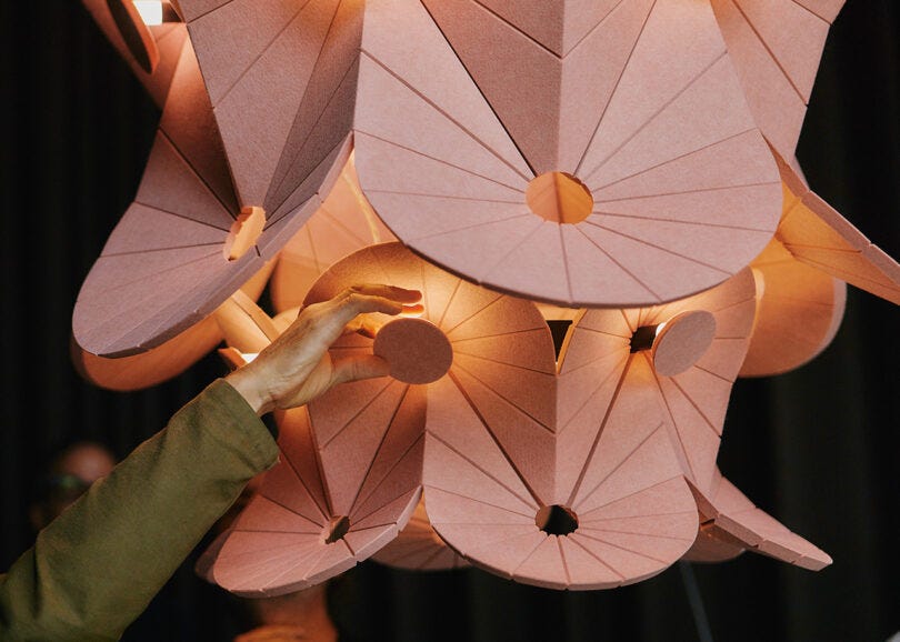 hands examining a pink felt acoustic chandelier