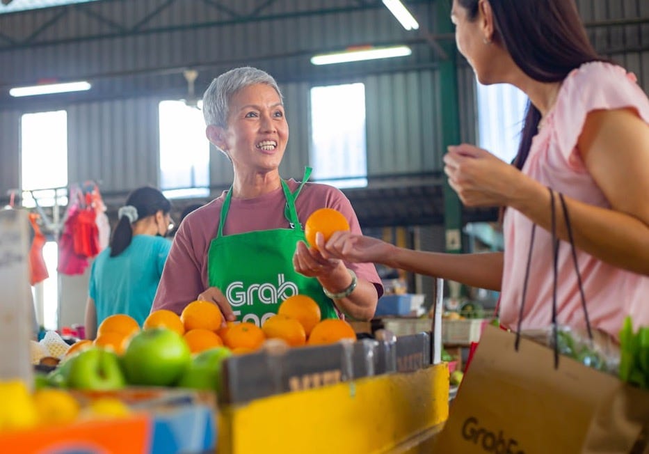 a woman in a green apron standing in front of a table filled with oranges