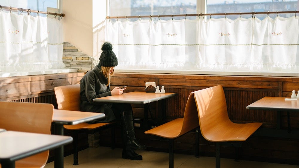A person sits alone in a restaurant looking down at their phone. A person sits alone in a restaurant looking down at their phone.