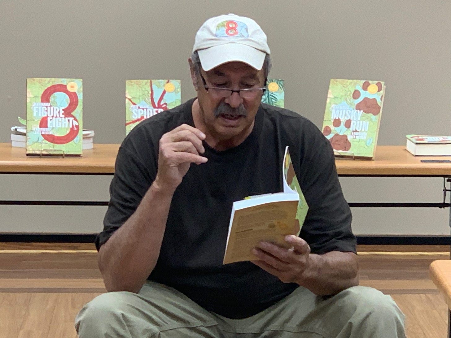 Jeff Nania sitting in a chair reading from a book.