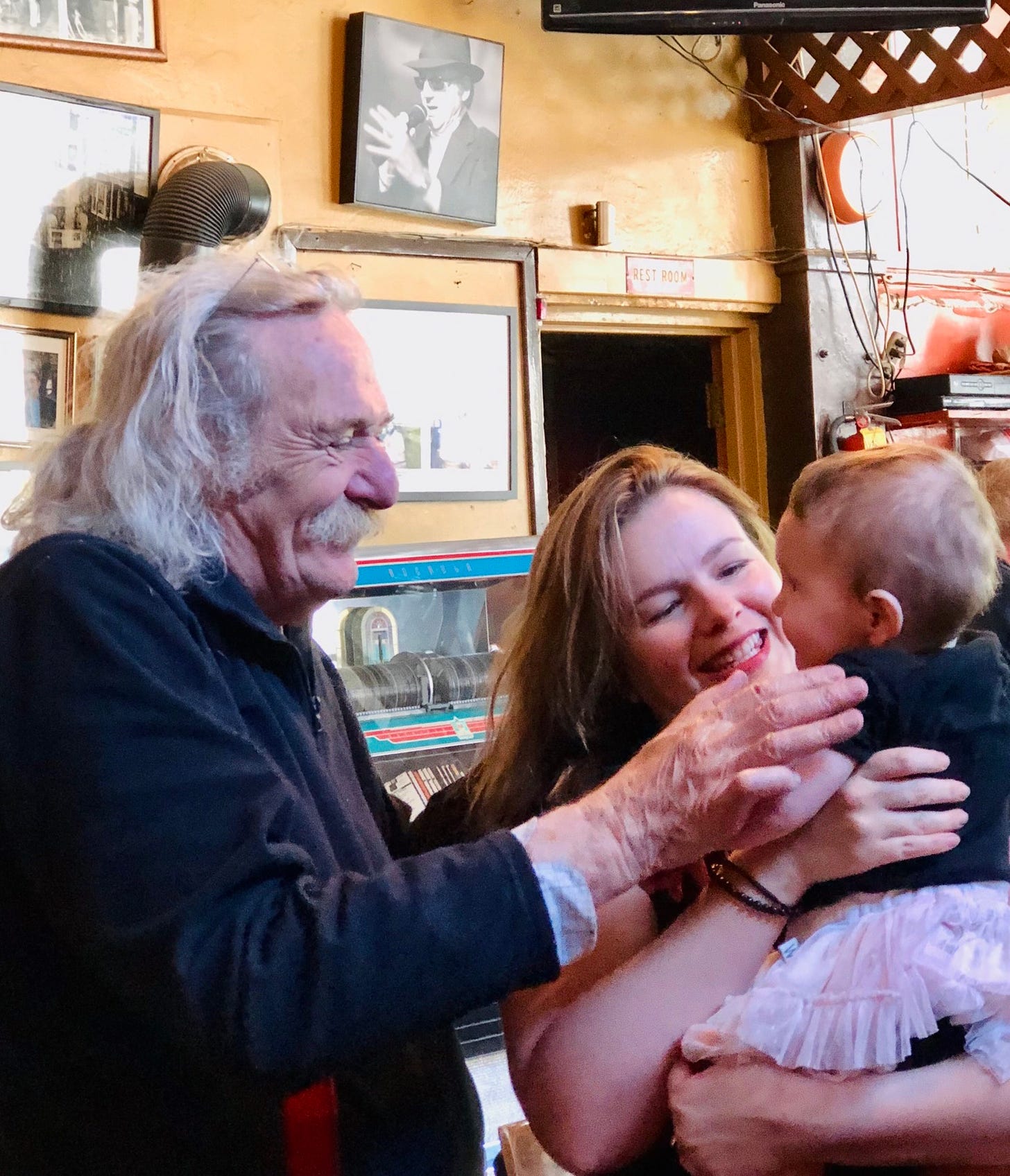 Jack Hirschman and Amber Tamblyn stand next to each other. Amber holds her infant daughter, Marlow, in her arms. Amber and Jack smile at Marlow as Jack puts his hand on Marlow's arm.