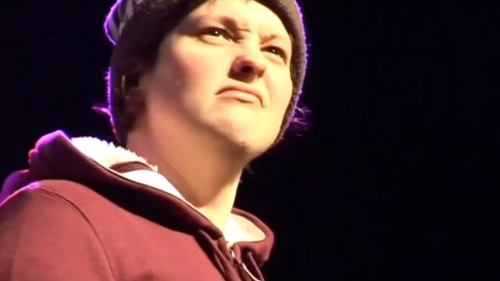 A woman in a beanie looks confused and annoyed on  a stage