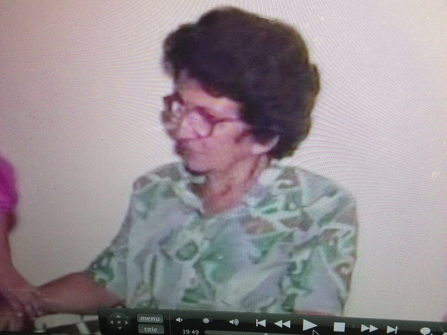 uma foto de minha avó, uma senhora de cabelos curtos e escuros, usando óculos e uma camisa estampada. a imagem não está nítida, é uma foto de uma tela de notebook