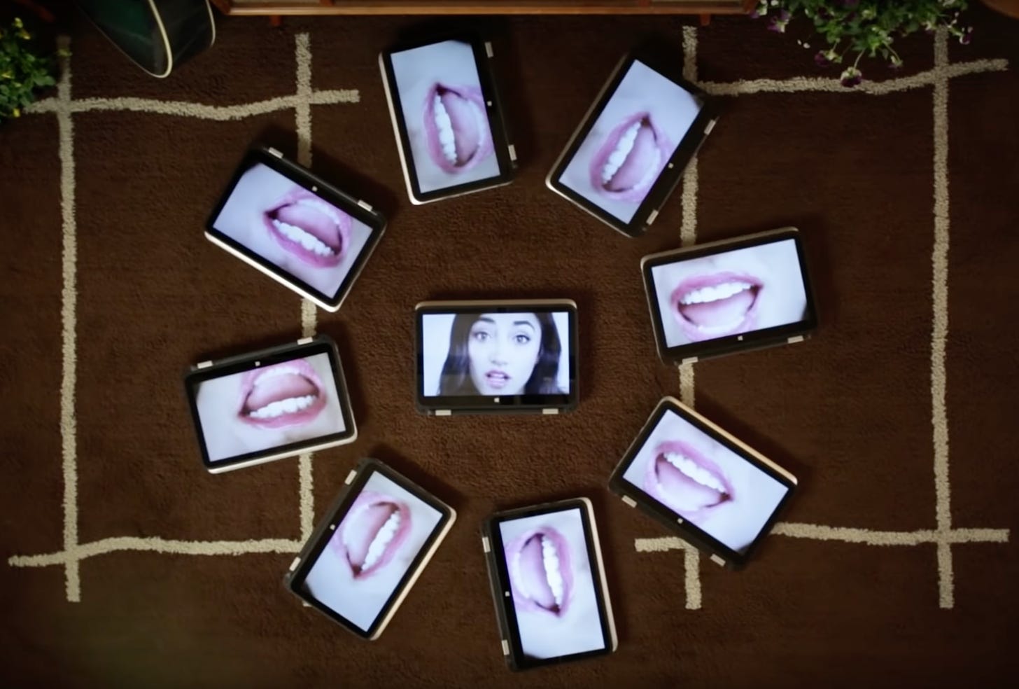 Several HP tablets arranged in a circle. All the external tablets have incredibly close up images of a mouth. A single tablet in the middle has an image of a brown haired girl looking doe-eyed.