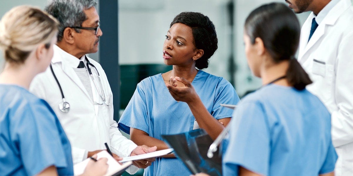 A Black medical professional is standing in a group, talking to her colleagues.