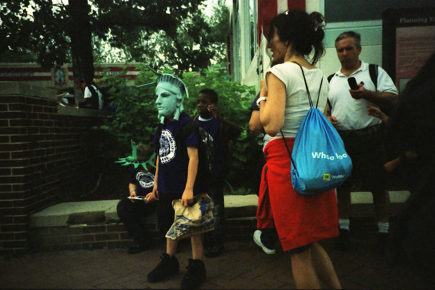 A boy wears a Statue of Liberty mask while a woman stands nearby.