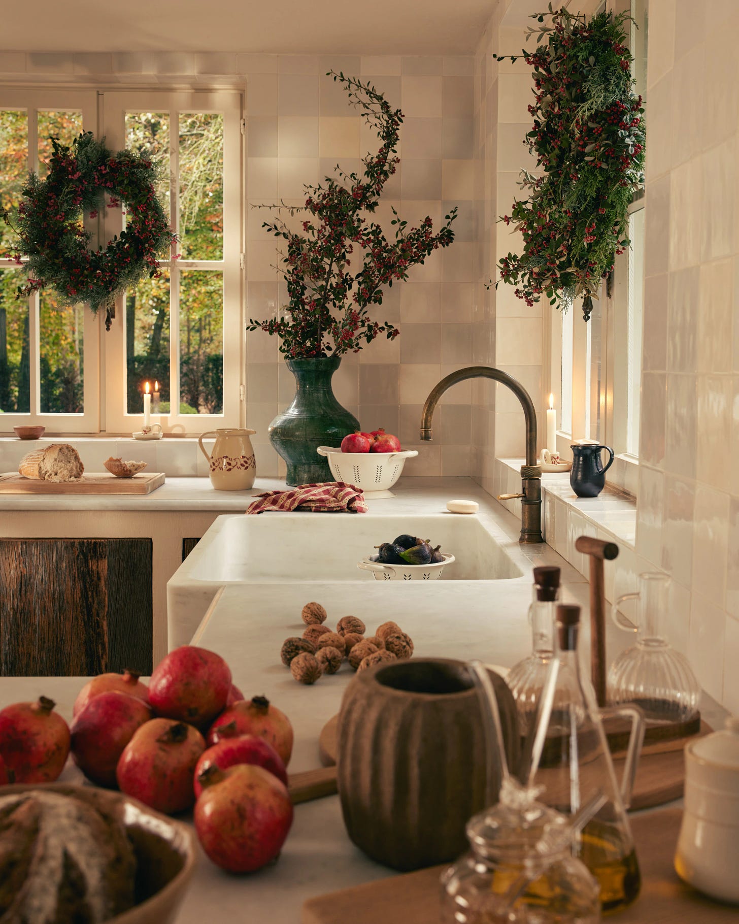 A festive kitchen with wreath, florals, candles, and produce strewn throughout.