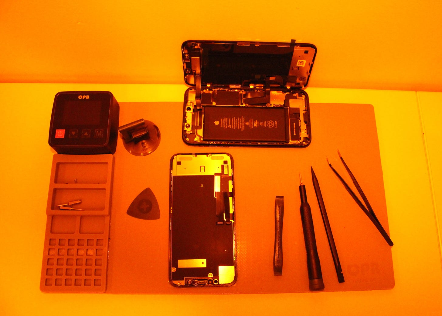 A photograph of a partially disassembled iPhone with repair tools.