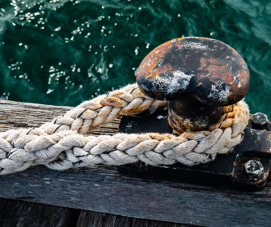 a rope looped over a rusty cleat on a weathered wooden dock over the green water