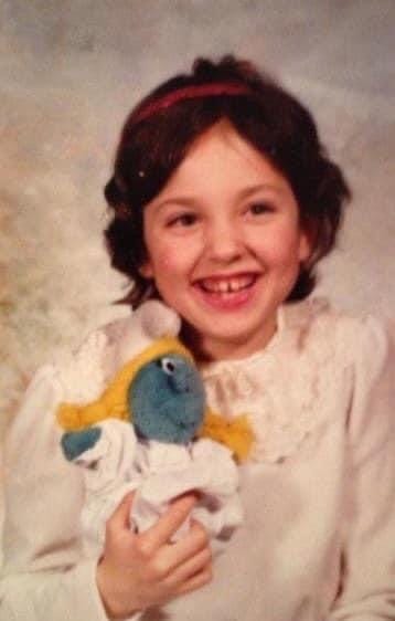 A cute picture of young Dia smiling, holding a little Smurfette plushie.