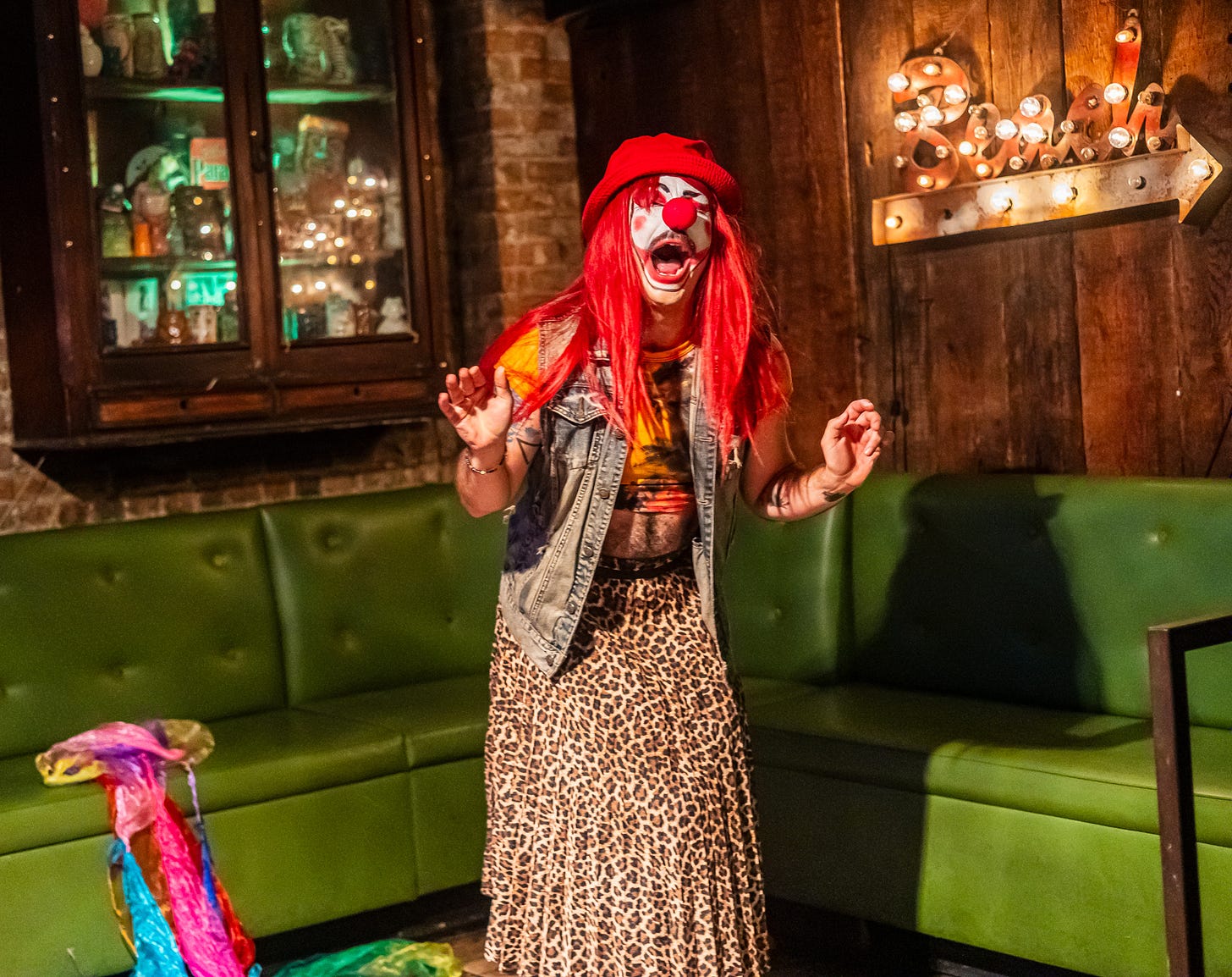 babz in long red wig and clown makeup and nose makes dramatic face onstage at queers n peers variety show