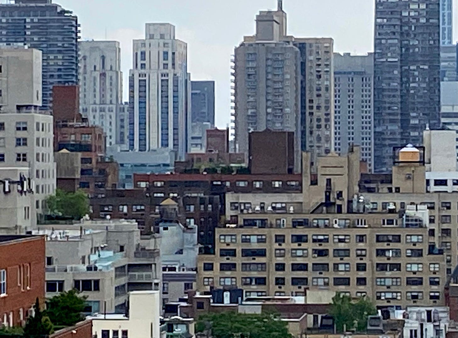 A city skyline with residential buildings of varying heights. 7 water towers can be seen on the roofs, some concealed behind masonry.