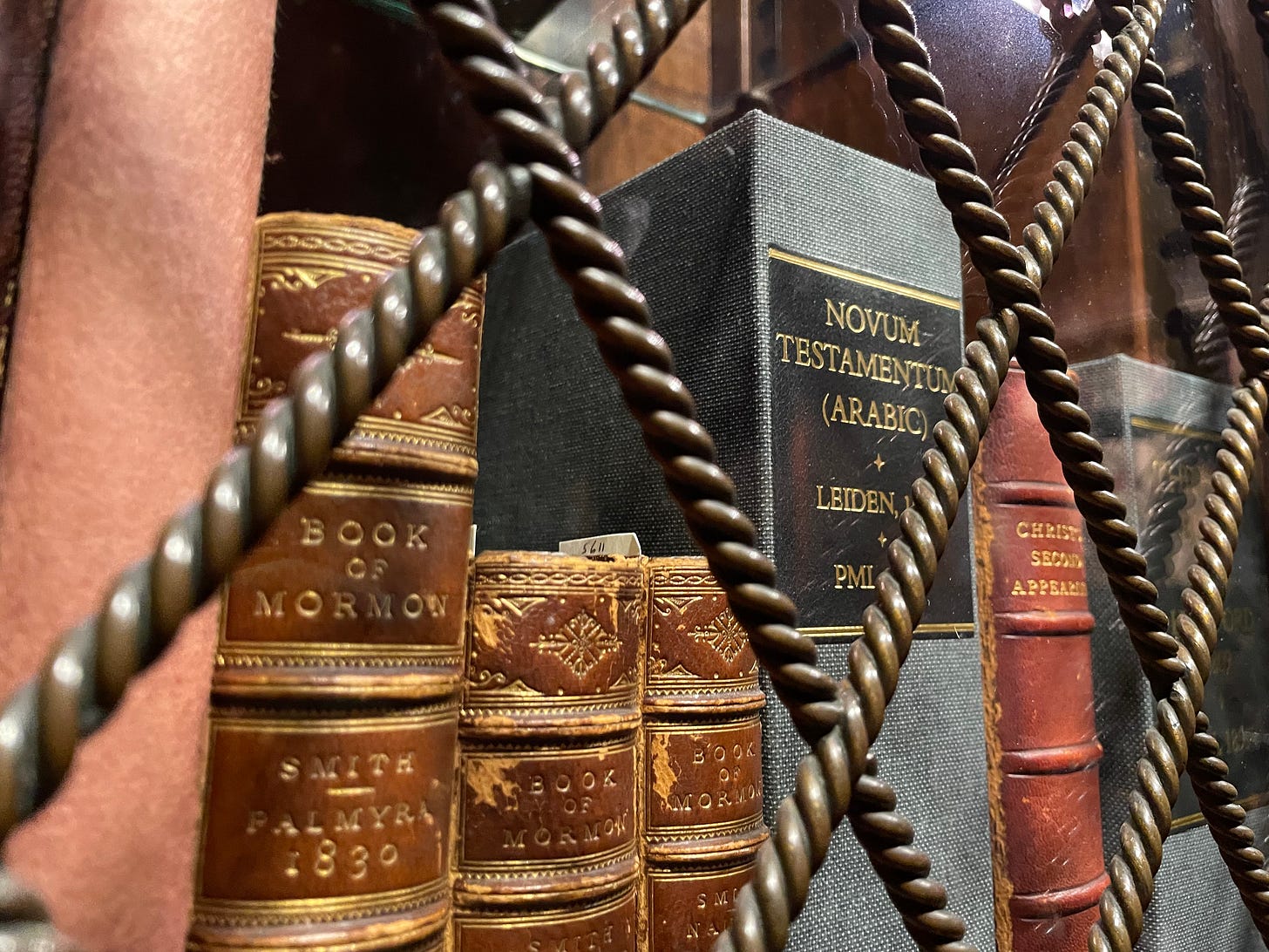 Old religious books sit behind glass and metal wiring, including the New Testamant in Arabic, and the Book of Mormon from 1830