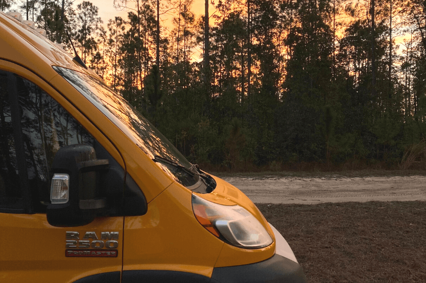 Hermes, a bright yellow converted Ram Promaster, sits on a forest road in front of an early morning sunrise