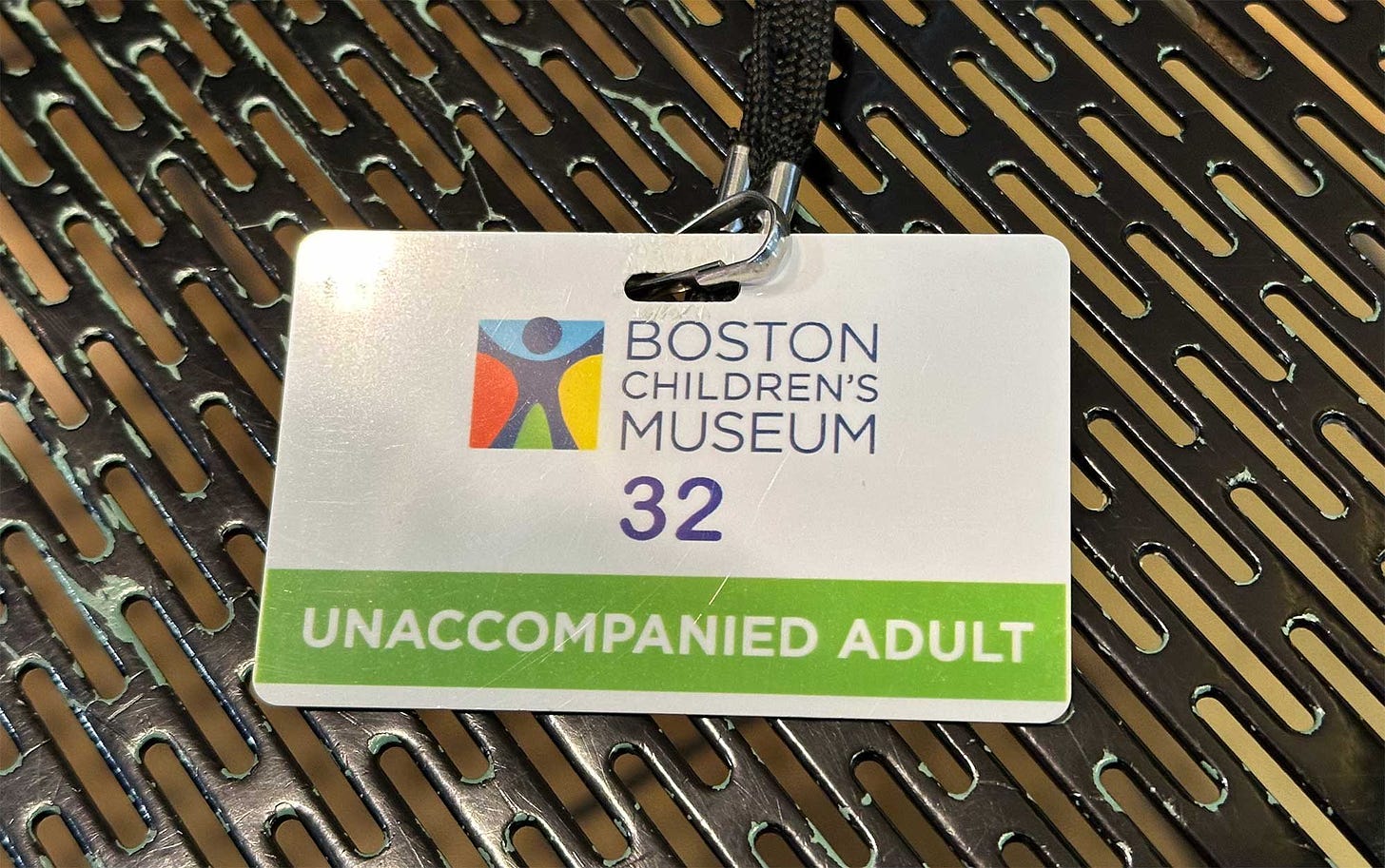 Plastic badge that has museum logo and the words Unaccompanied Adult written in large bold print.