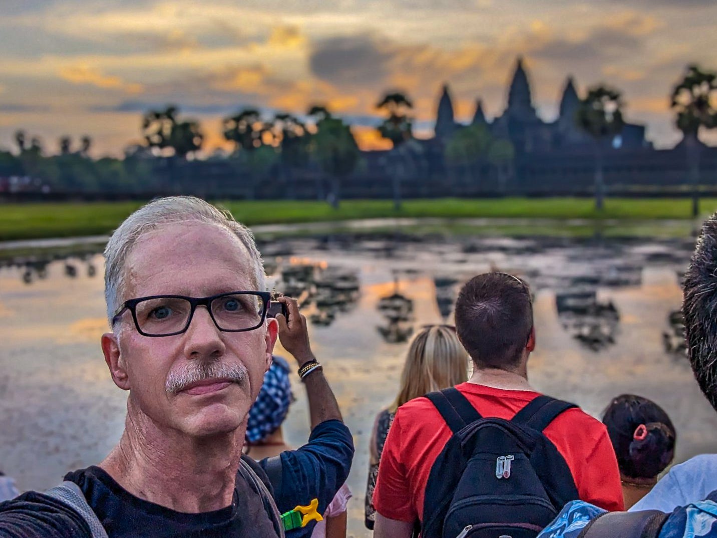 Michael standing in front of Angkor Wat, which is reflected in the water as the sun rises. 
