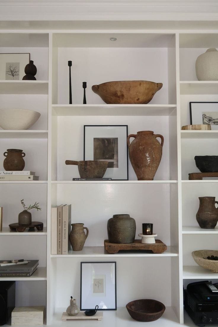 This may contain: shelves with vases, bowls and other items on them in a white walled room