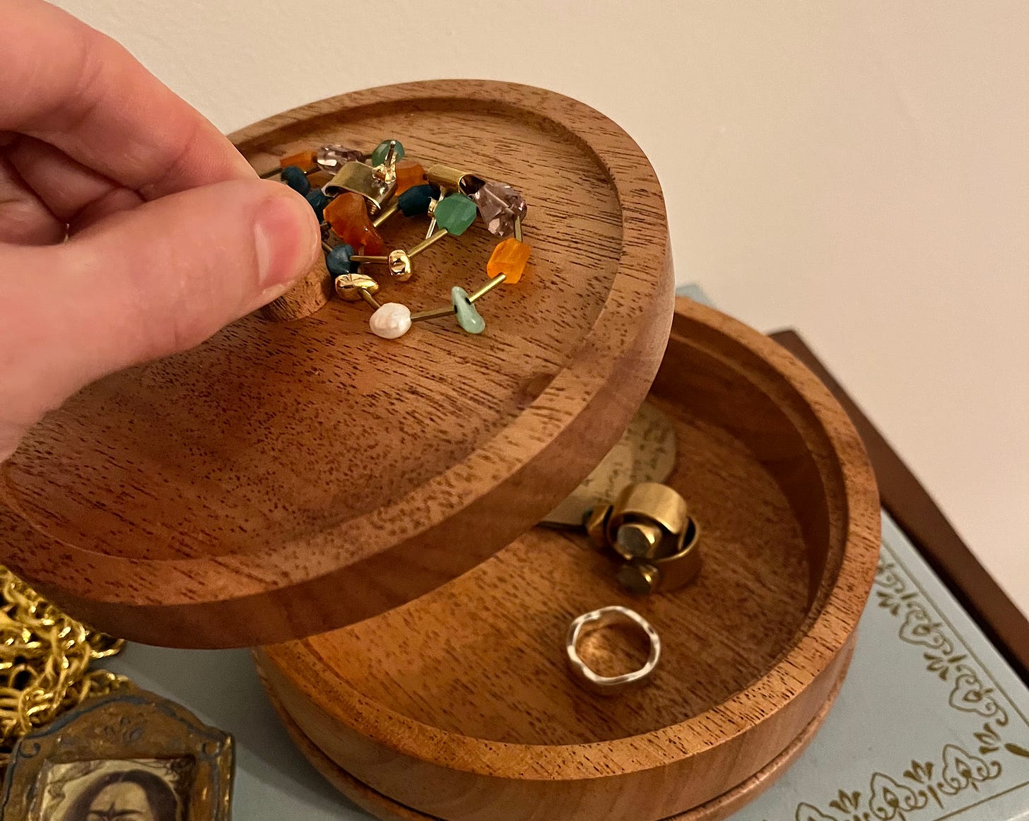 Box with colourful earrings on top, a hand removing the lid to reveal more jewellery inside.