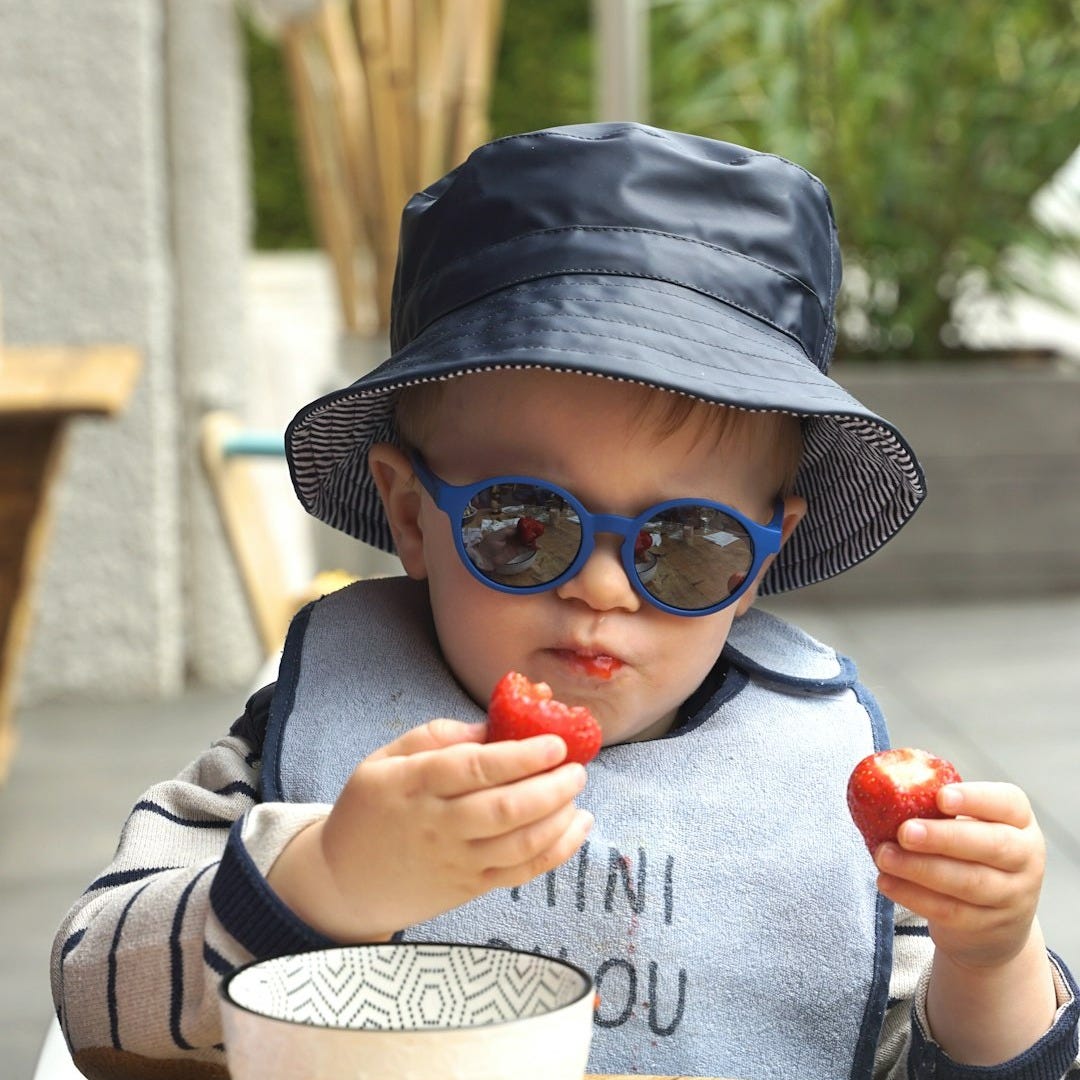 a baby wearing sunglasses and a hat eating a strawberry a baby wearing sunglasses and a hat eating a strawberry