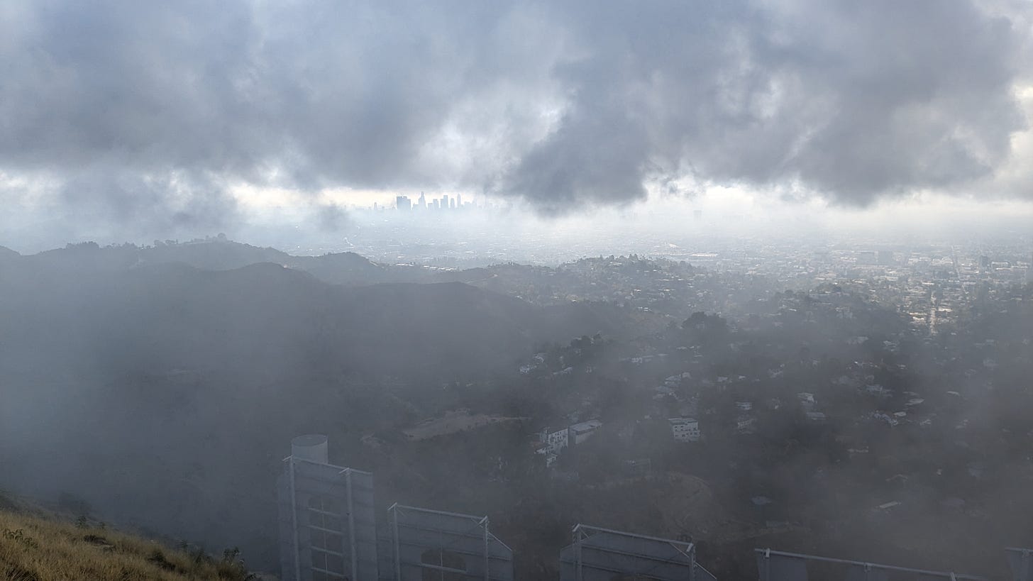 in the distance, skyscrapers, in the foreground, sloping hills and the last few letters of the Hollywood sign