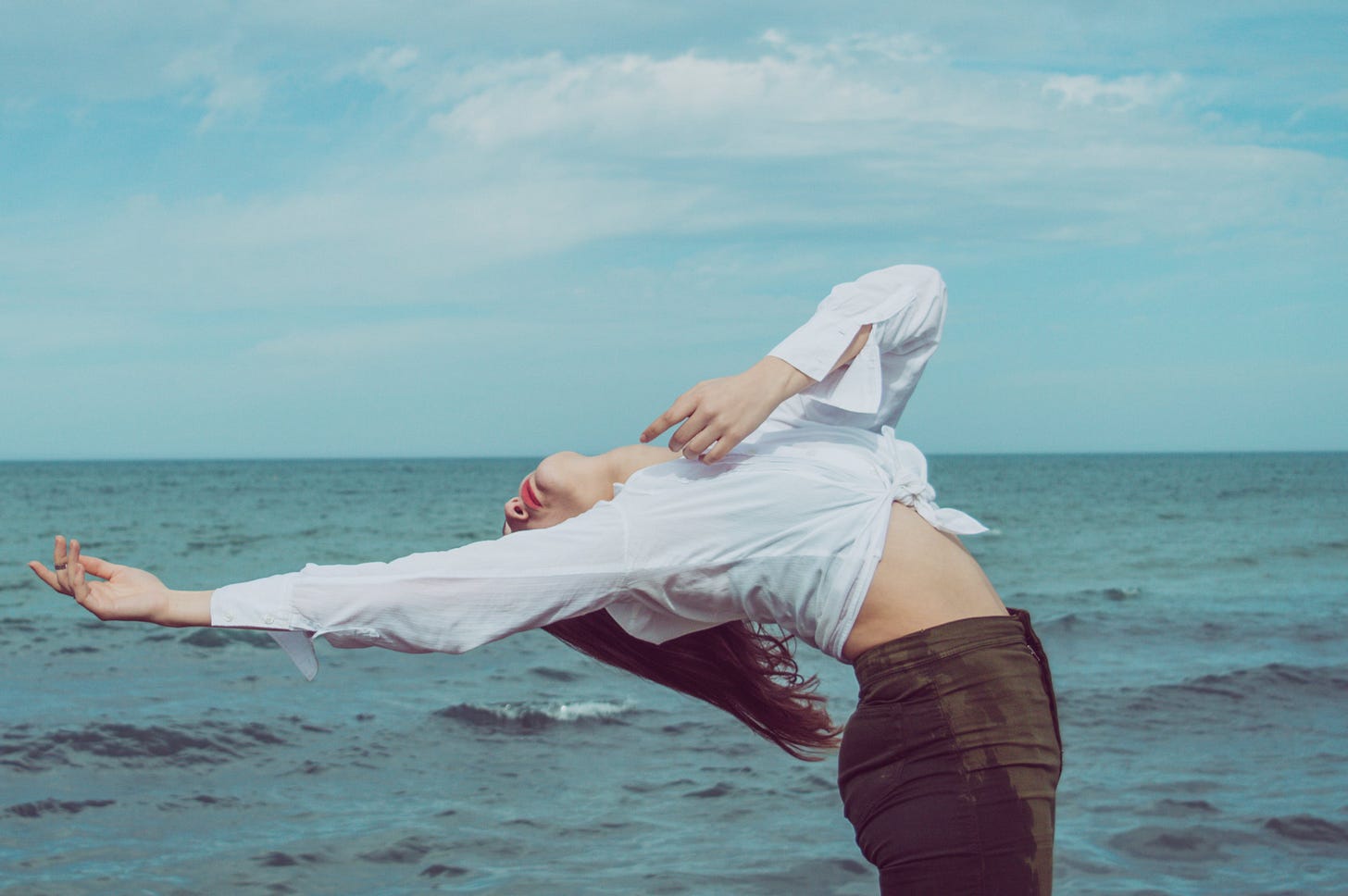 Woman bends backwards gracefully in front of a backdrop of the ocean