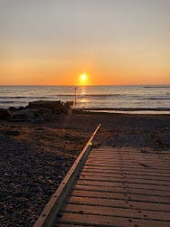 An orange sunset in a sky - the sun is setting in the centre of the picture. It's an empty beach, with a wooden jetty leading down to the sand. The tide is out and the water is glistening under the sun. It looks beautiful.