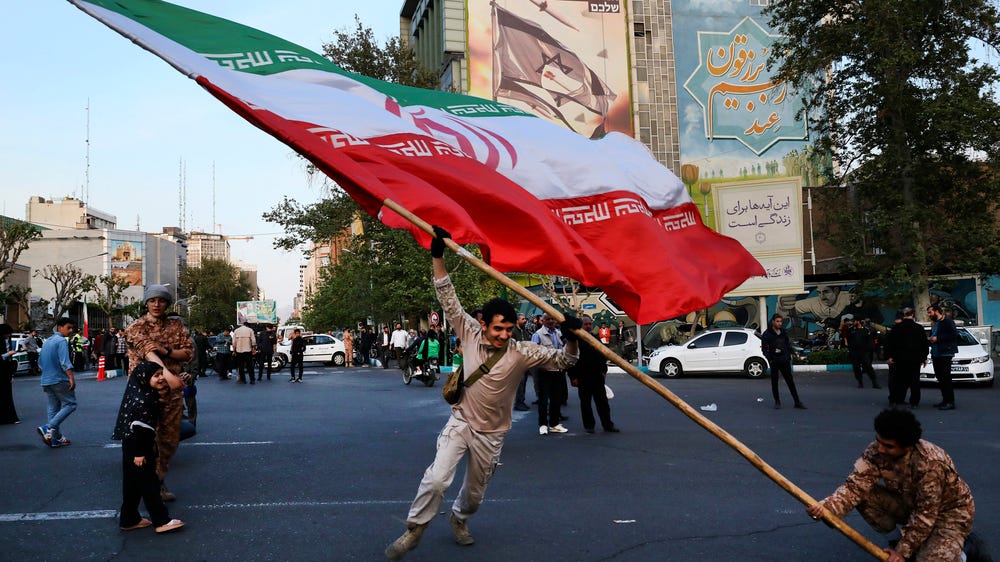 Demonstrators wave a huge Iranian flag in an anti-Israeli gathering in front of an anti-Israeli banner on the wall of a building at the Felestin (Palestine) Sq. in Tehran, Iran, on Monday, April 15, 2024. (AP)