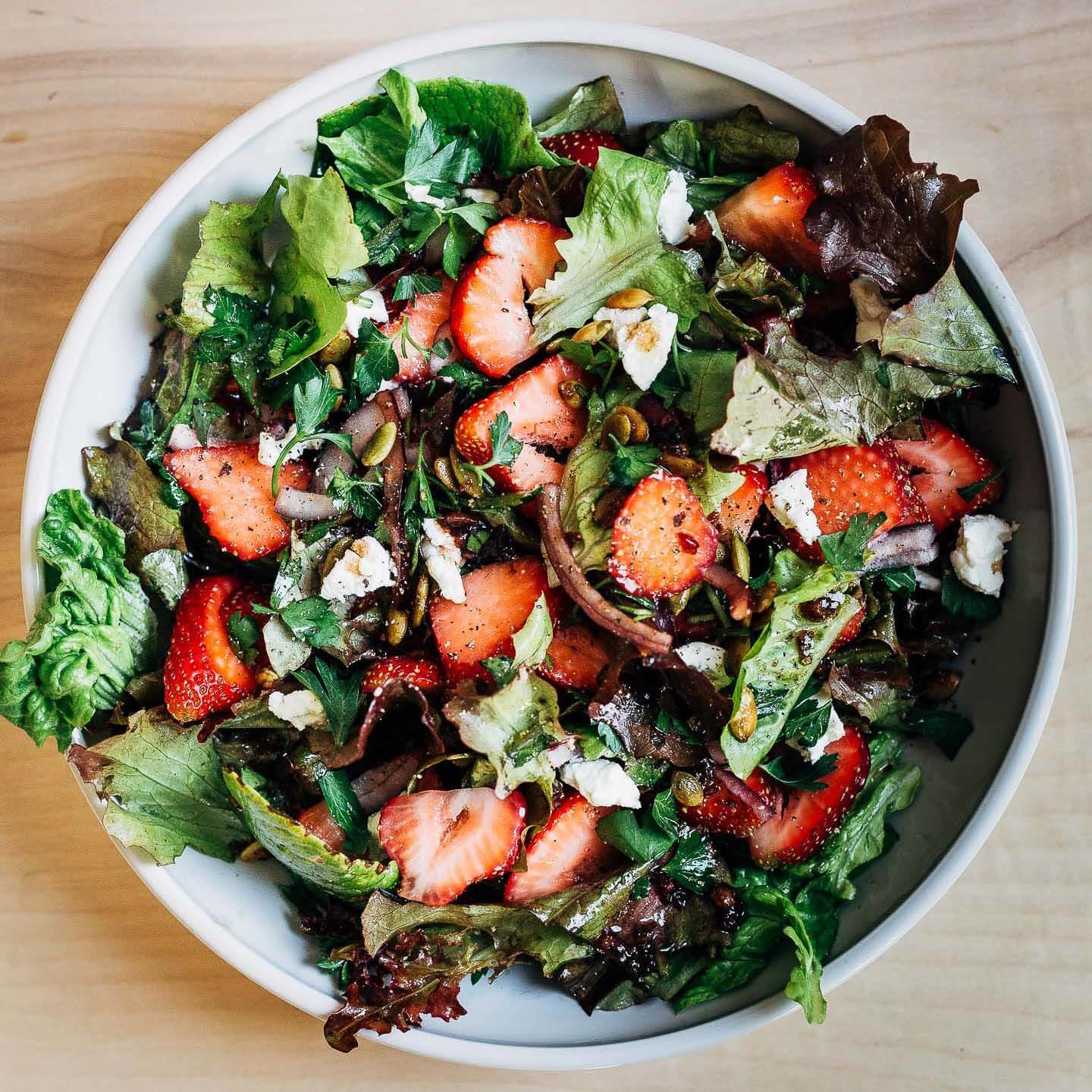 A big, wide bowl filled with salad greens, strawberries, and pepitas. 