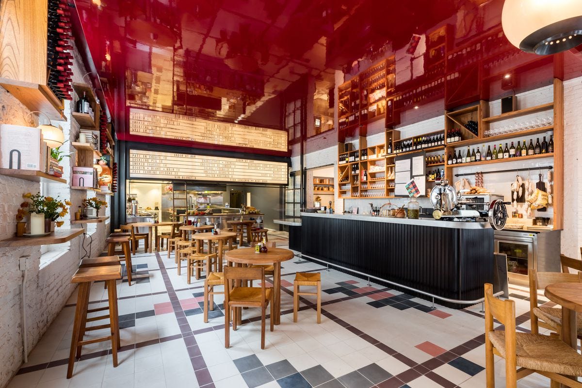 The interior of a wine bar, with tiled floors, a red ceiling, a long bar to the right, and high tables with high chairs. 