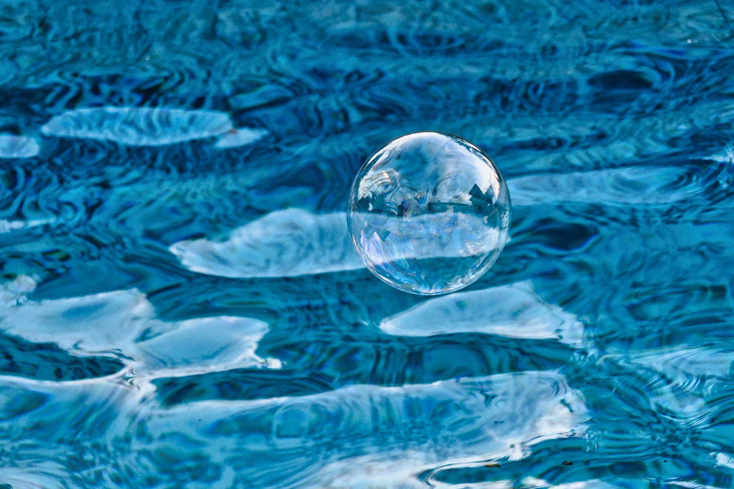 A soap bubble floats above the water in the pool; the reflection of the sun creates a bright blue background