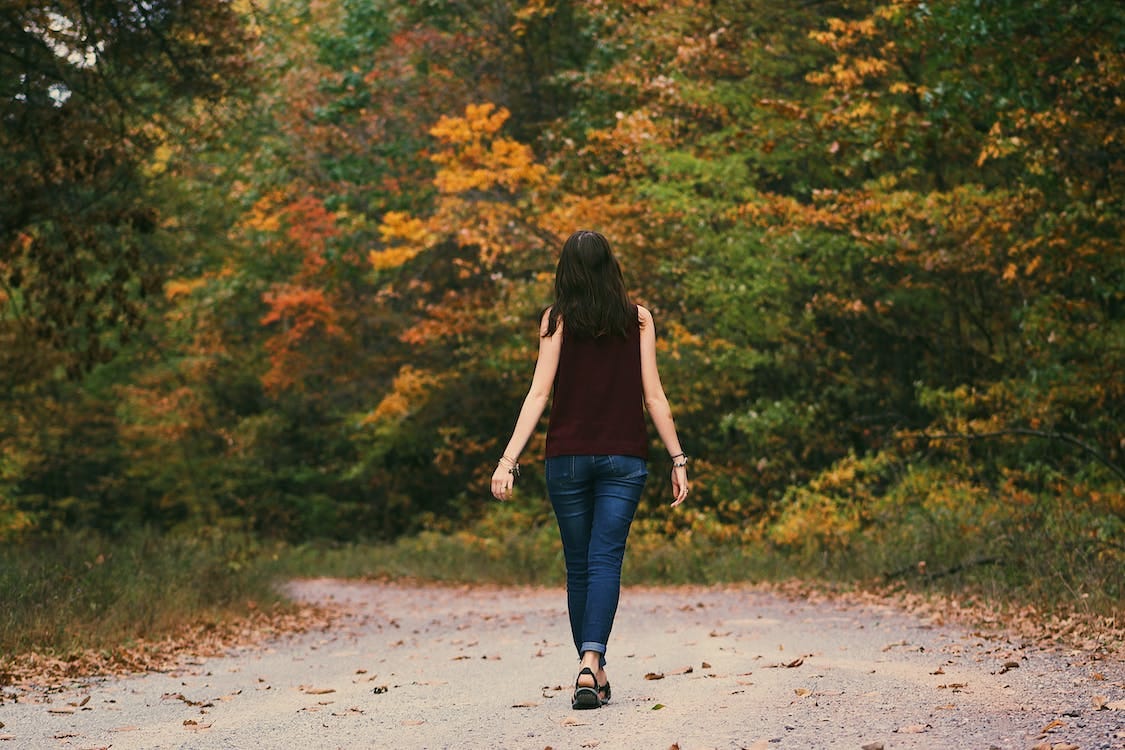 Free Woman in Brown Sleeveless Dress and Blue Jeans Standing on Gray Path Road Stock Photo