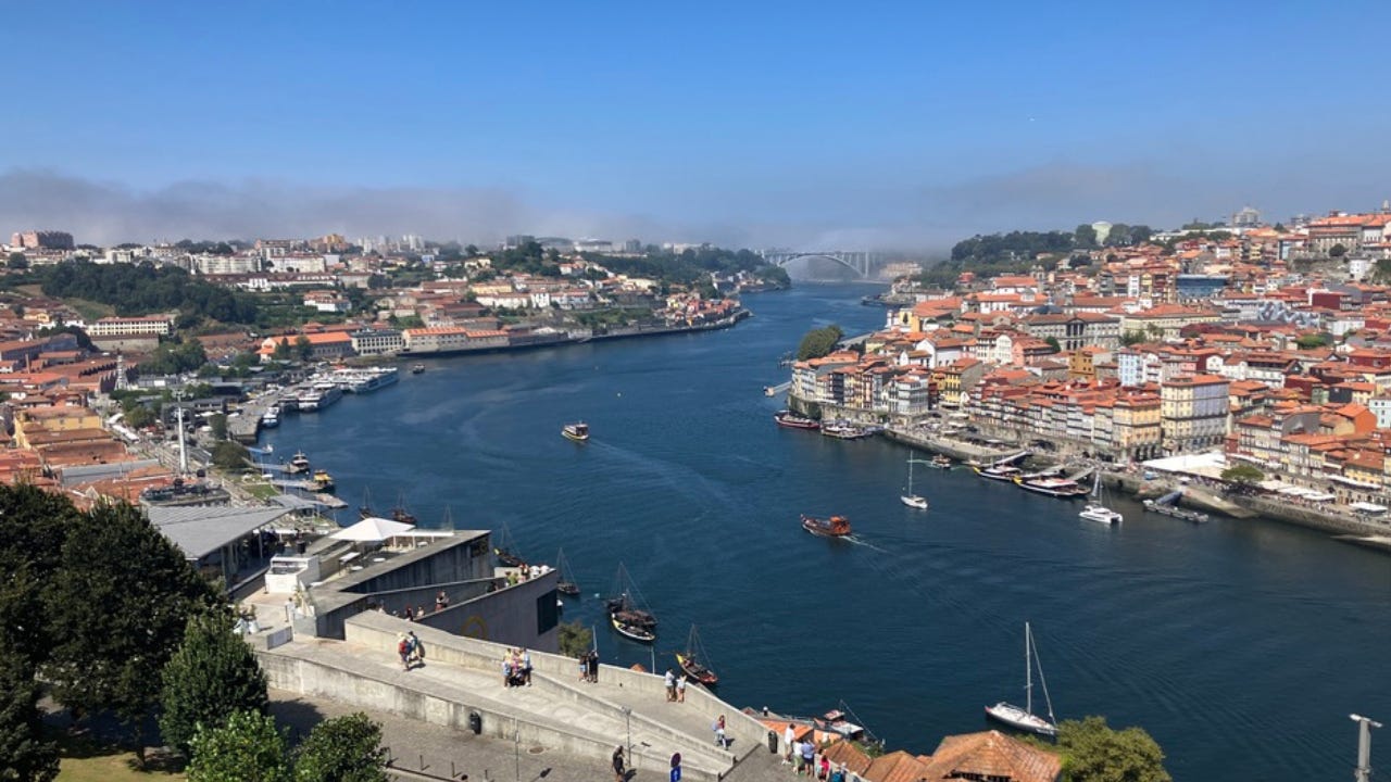 The Duoro River flowing through Porto with the historic port cellars on the left, the Ribeira on the right, and the marine layer coming in from the Atlantic over the Ponte da Arrábida.