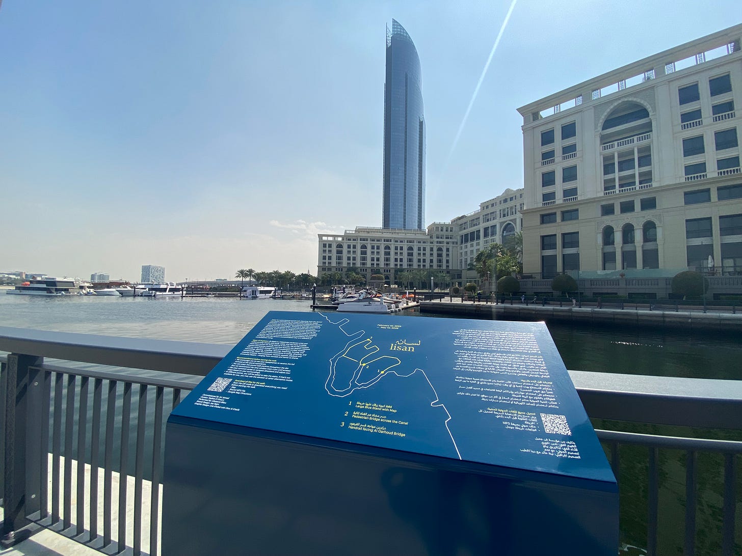 Photo of an blue sign on a ledge overlooking a view of the creek and a hotel and glass tower.