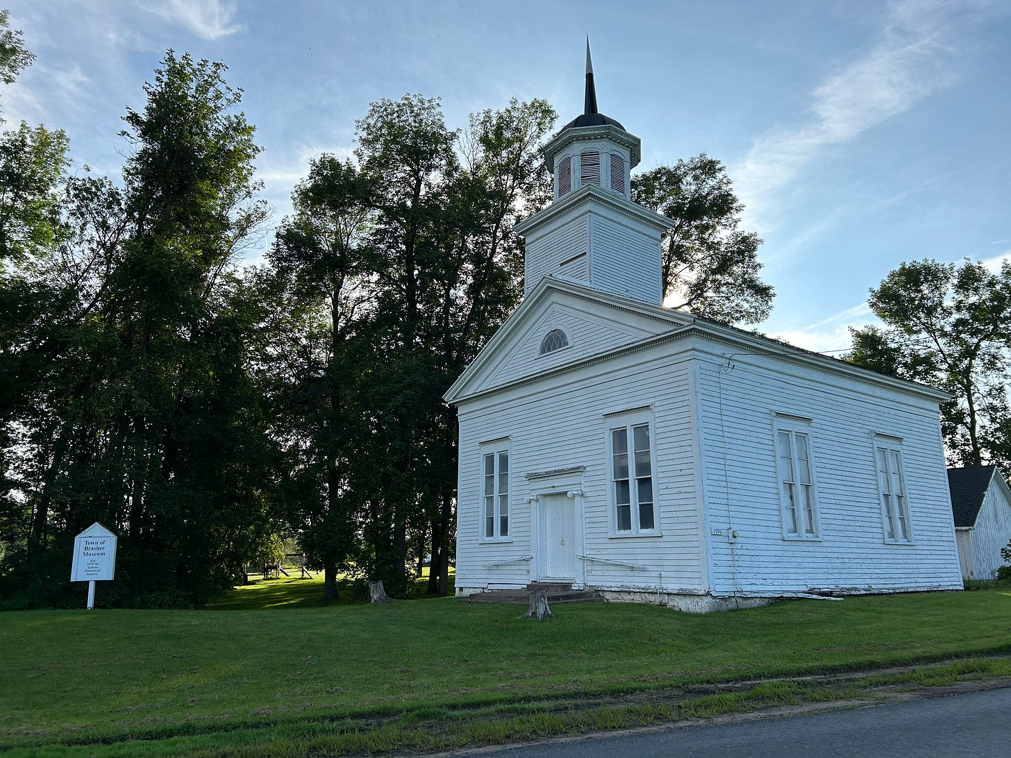 A small, abandoned white church sits on a bed of grass, slightly backlit by the setting sun. 