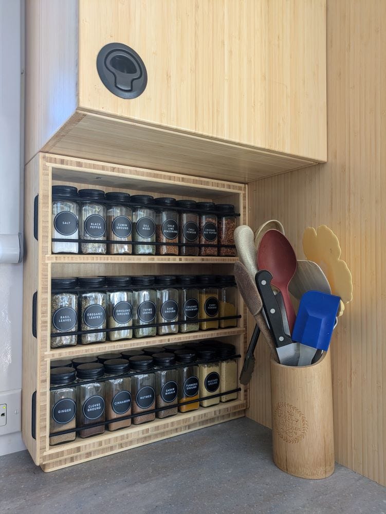 a bamboo spice rack filled with glass jars of spices, mounted on a counter top beneath other matching bamboo cupboards